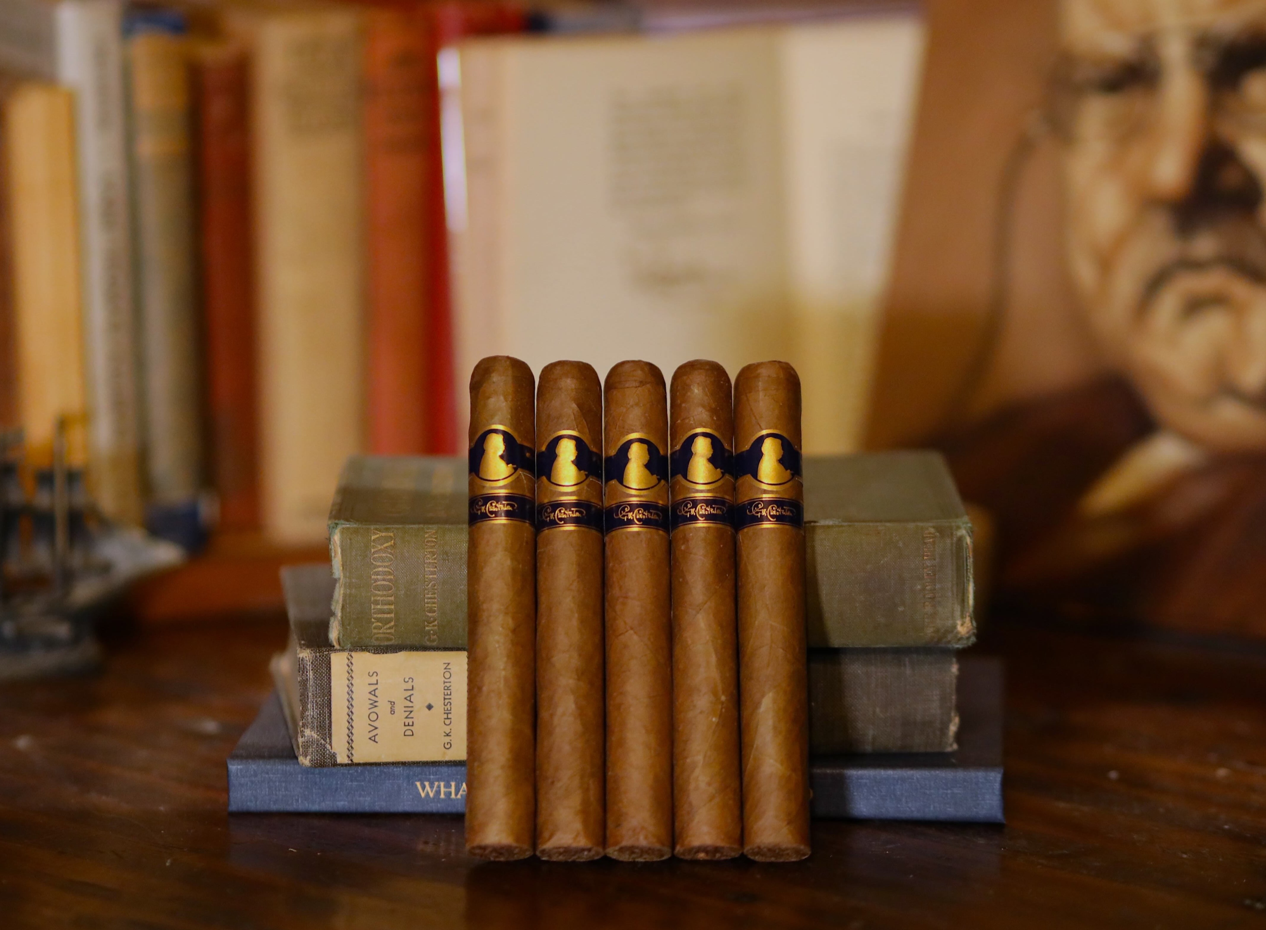 Stack of cigars on a wooden surface with books and a portrait in the background
